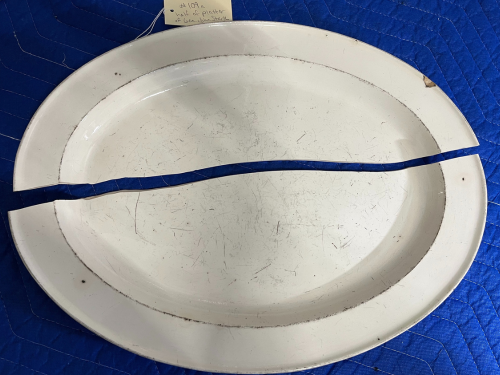A broken white ceramic platter with a note attached, placed on a blue surface.