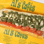 A sandwich with pesto, chicken, and tomatoes on a sub roll labeled Al's Cafés. Considered among places to eat downtown crossing.