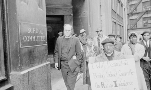 People are seen protesting for racial balance in education, highlighting education equality outside a school committee building.