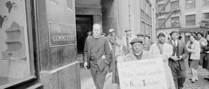 People are seen protesting for racial balance in education, highlighting education equality outside a school committee building.