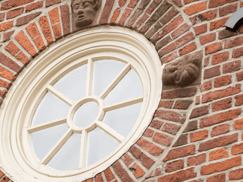 Circular window with ivory trim set into a brick wall