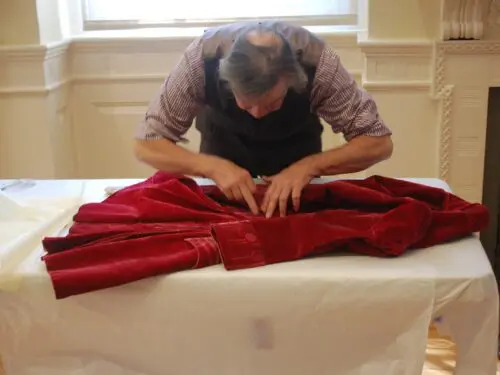 A person is meticulously adjusting a luxurious red coat on a table, focusing intently on the details.