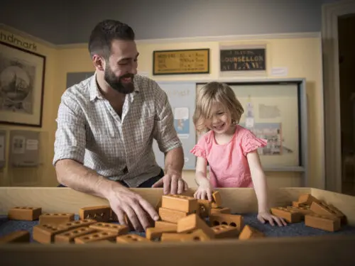 A man and a child are playing with toy bricks at an exhibit, likely at the Old South Meeting House Hands-On History Days.