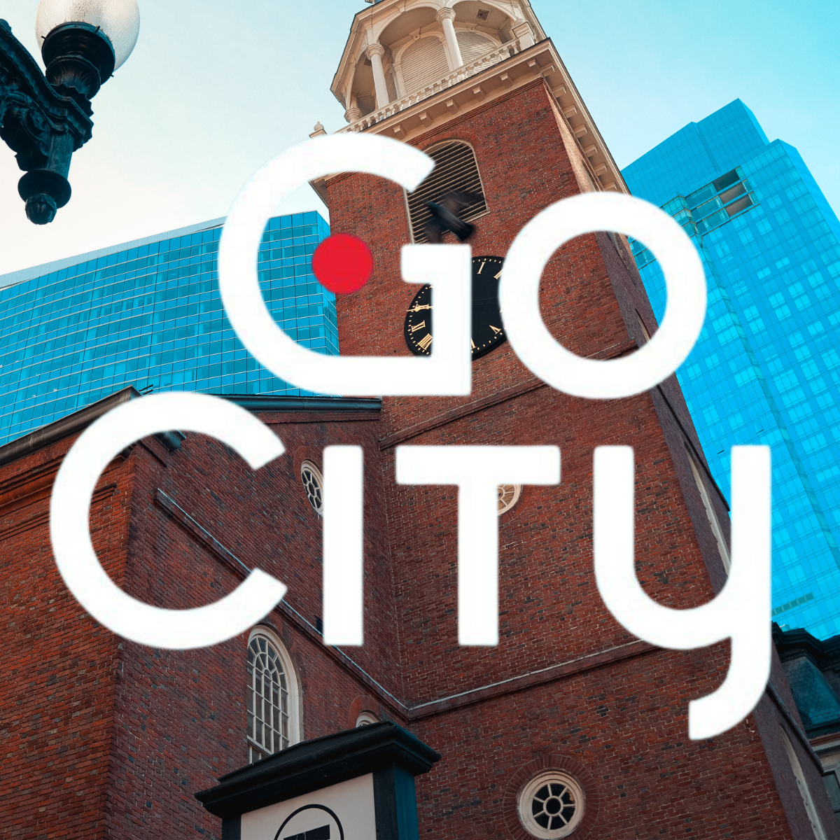 A tall brick building with a clock tower and modern skyscrapers, featuring "Go City." Suitable for Boston sightseeing.