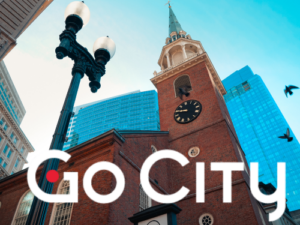 A tall brick building with a clock tower and modern skyscrapers, featuring "Go City." Suitable for Boston sightseeing.