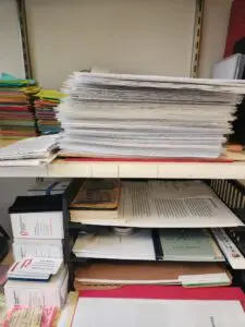 Stacks of paper on a desk, including sticky notes, business cards, and regular paper