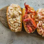Three seafood rolls on a wooden board, featuring crab, lobster, and shrimp.