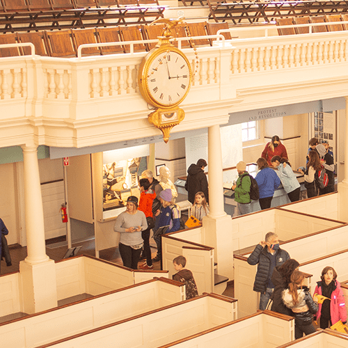 People are exploring an interior with a vintage clock and historical displays, possibly the Old State House in Boston.
