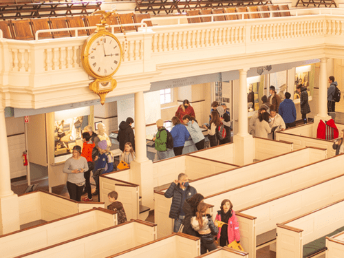 People are exploring an interior with a vintage clock and historical displays, possibly the Old State House in Boston.