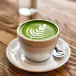 A cup of matcha latte with latte art on a wooden table.