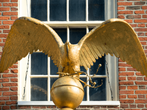 A golden eagle sculpture with wings spread sits atop a globe, set against a brick building.