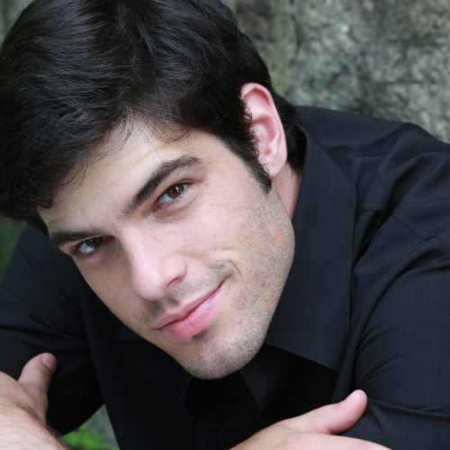 A person wearing a black shirt is looking toward the camera while outdoors.