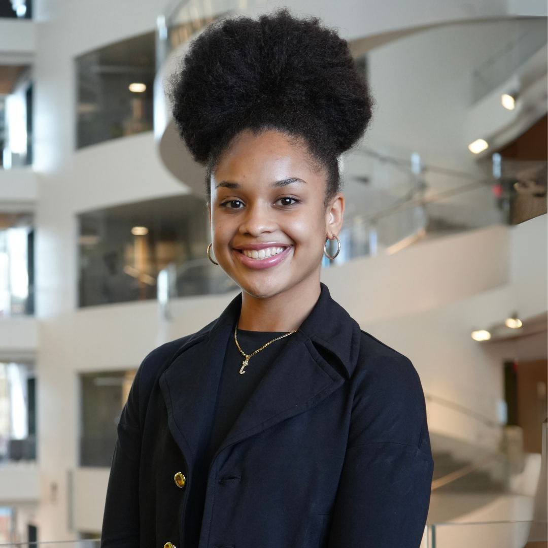 A person is smiling indoors, with a modern architectural background featuring curved staircases.