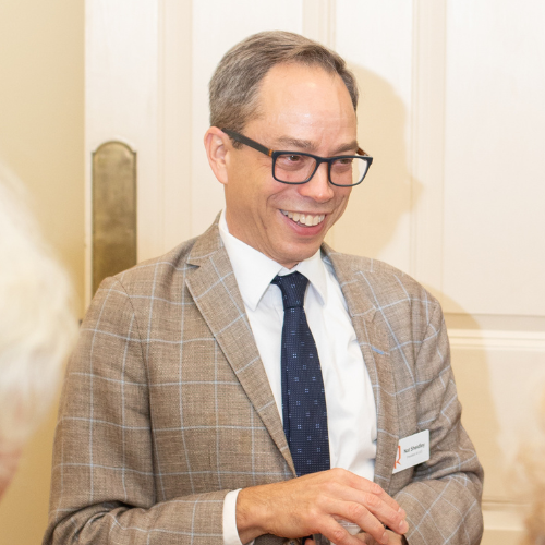 A person in glasses and a suit smiling in a well-lit room.