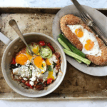 A skillet with eggs, vegetables, and cheese, and a plate with eggs on bread, accompanied by cucumber slices.