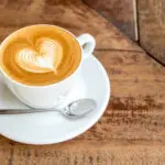 A cappuccino with latte art in a white cup on a wooden table.