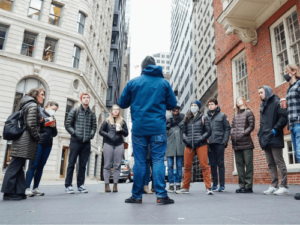 A group of people stand in a city street, on a tour.