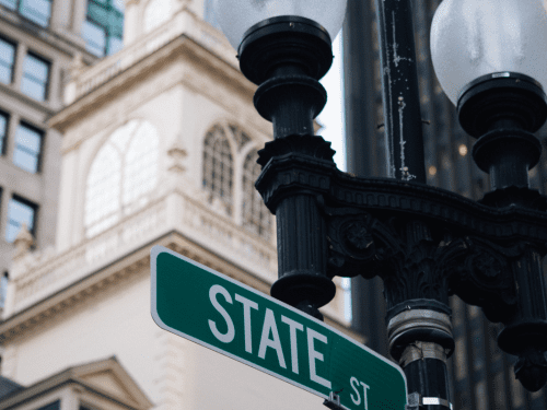 A street sign for State Street is seen with ornate lamp posts and historic architecture visible in the background.