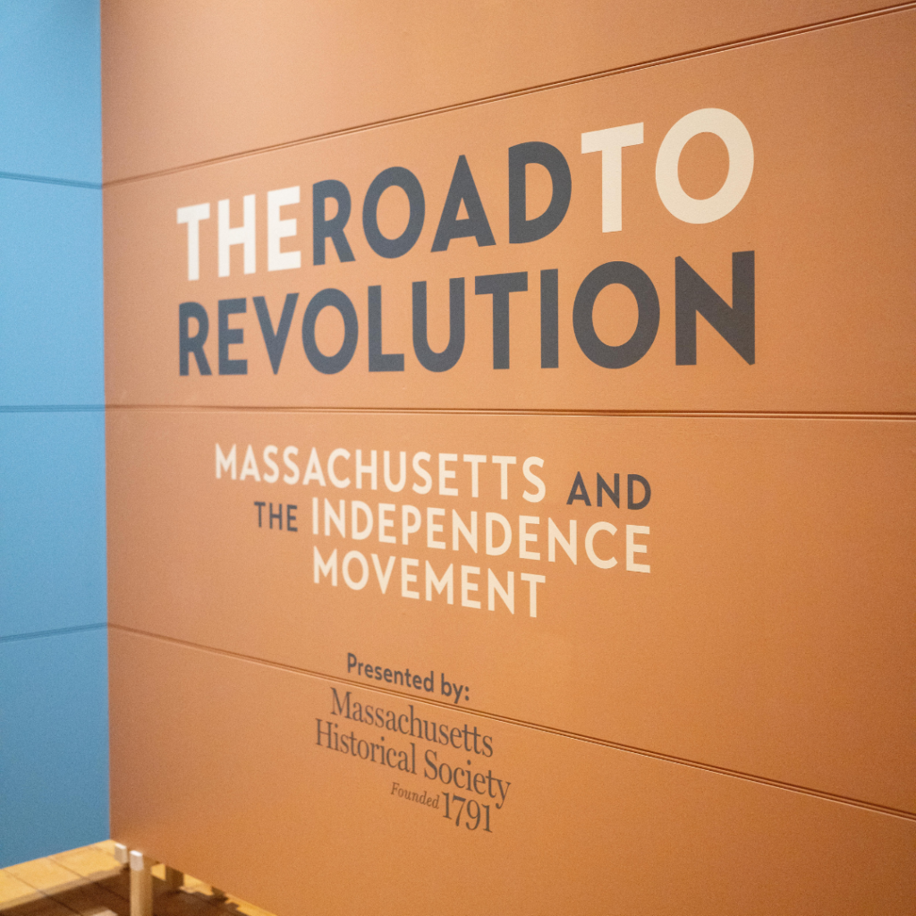 Exhibit wall with text saying "The Road to Revolution: Massachusetts and the Independence movement" presented by Massachusetts Historical Society founded 1971