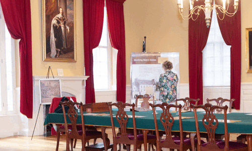 Room featuring colonial-style decor and a long table as well as tall windows and exhibits