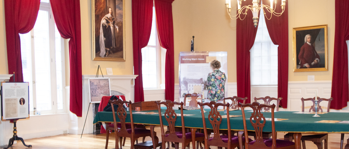 Room featuring colonial-style decor and a long table as well as tall windows and exhibits