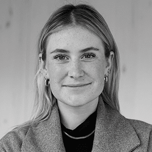 A person with long hair and earrings wearing a jacket, in a grayscale portrait photograph.