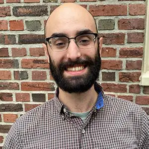 A person is smiling in front of a brick wall.