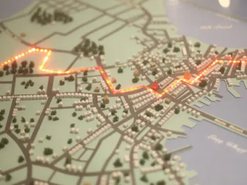 A lit-up map displays streets and buildings, highlighting a particular route. It resembles a model for city navigation or planning in relation to Revolutionary Spaces directions.