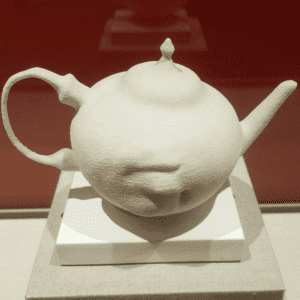Plaster teapot with the shape of a human mouth extending from the body.